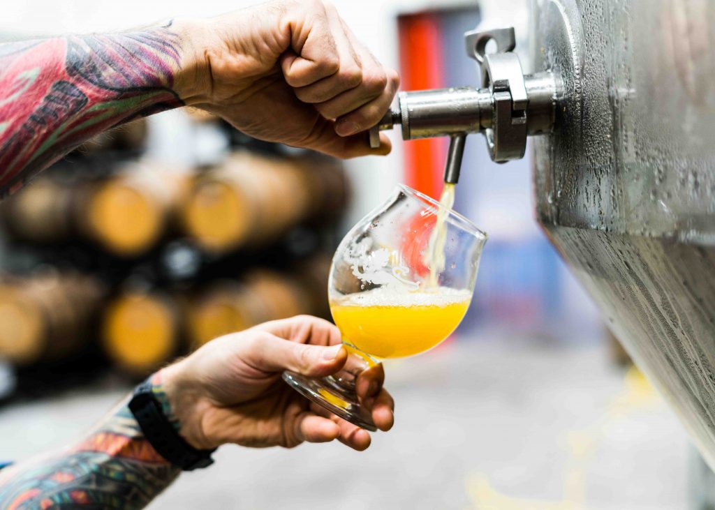 Photo of a hand filling a glass of beer from an industrial beer tank