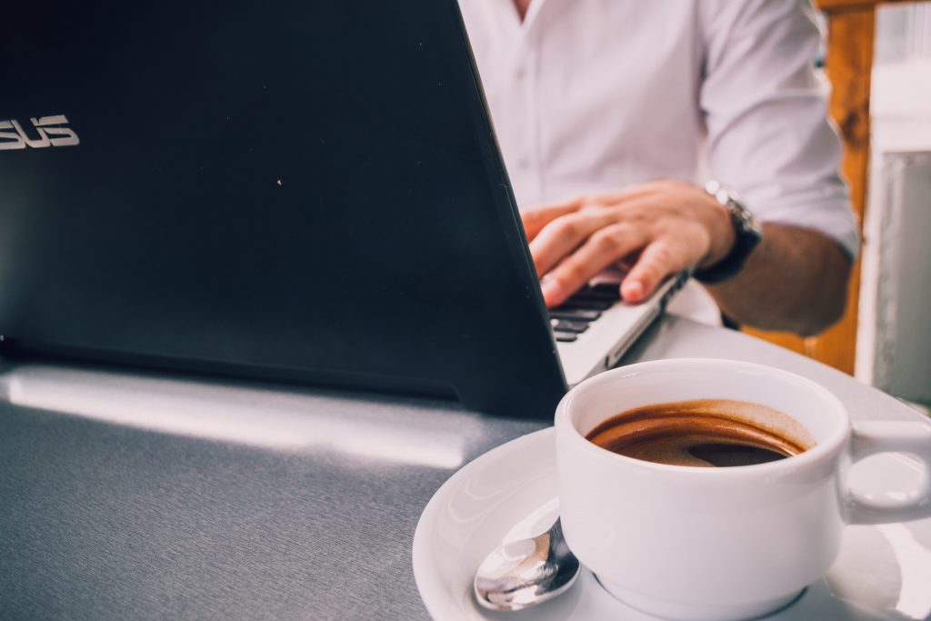 Person typing at a laptop with an espresso