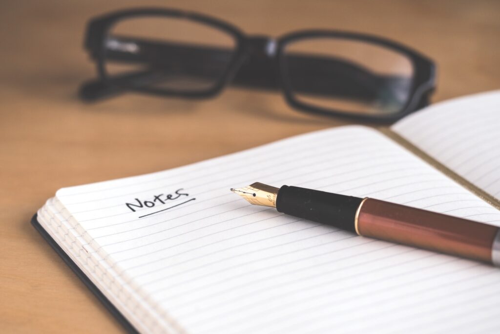 Break through at a conference by taking detailed notes of your target speakers. Here you see a fountain pen sitting on an open notebook in front of a pair of glasses.